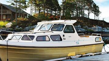 A small, white motorboat docked at a pier with a rocky shoreline and trees in the background.