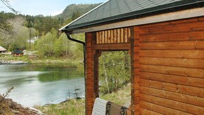 A wooden cabin with a porch overlooking a river, surrounded by greenery and hills. - 5 Person Holiday Home in Vagland (Heim)