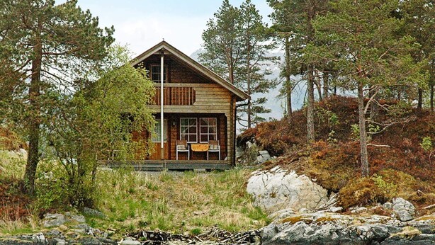 A cabin with a porch, surrounded by trees and a body of water. - 5 Person Holiday Home in Vagland (Heim)