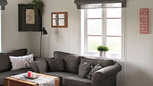 A cozy living room with a grey sofa, a small table with candles, a framed picture, and a window with a view. - 5 Person Holiday Home in Vagland (Heim)