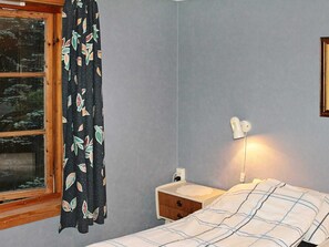 A bedroom with a bed, a nightstand, a lamp, a window with curtains, and a view of trees outside.