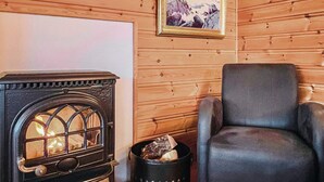Ein gemütliches Zimmer mit Kaminofen, einem schwarzen Ledersessel und einem gerahmten Bild an der Wand.