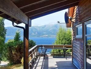 A wooden deck with a table and chairs, overlooking a lake with mountains in the background. - 4 Star Holiday Home in Leikanger (Sogndal)