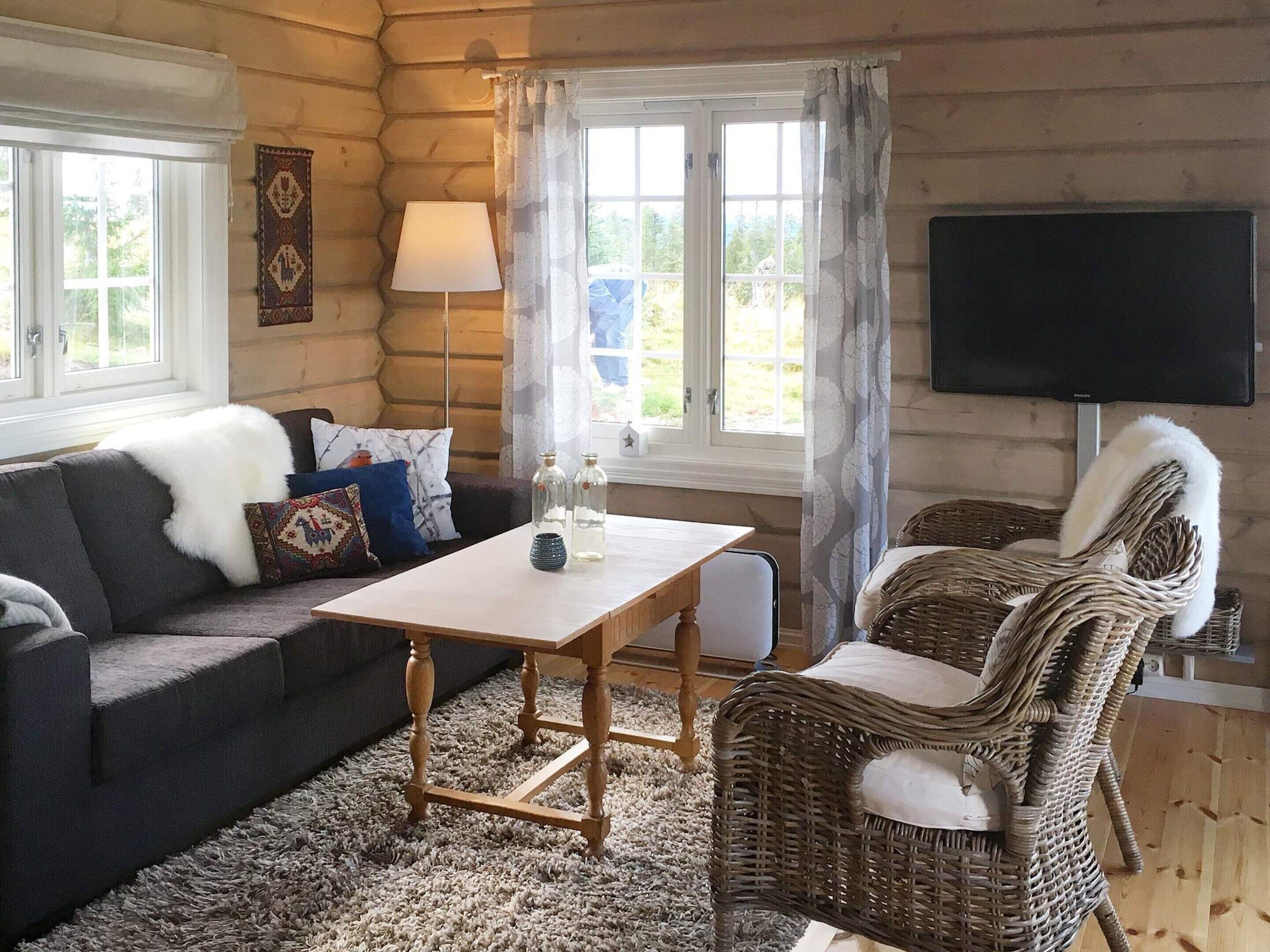 Interior de una cabaña de troncos con un sofá, una silla de mimbre, una mesa y un televisor.