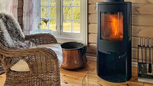 Una habitación acogedora con un ventanal grande, una chimenea, un sillón de mimbre y una olla de cobre.