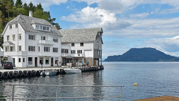 A waterfront property with a large white building, docked boats, and a wooden pier. - 4 Person Holiday Home in Bjoa (Vindafjord)