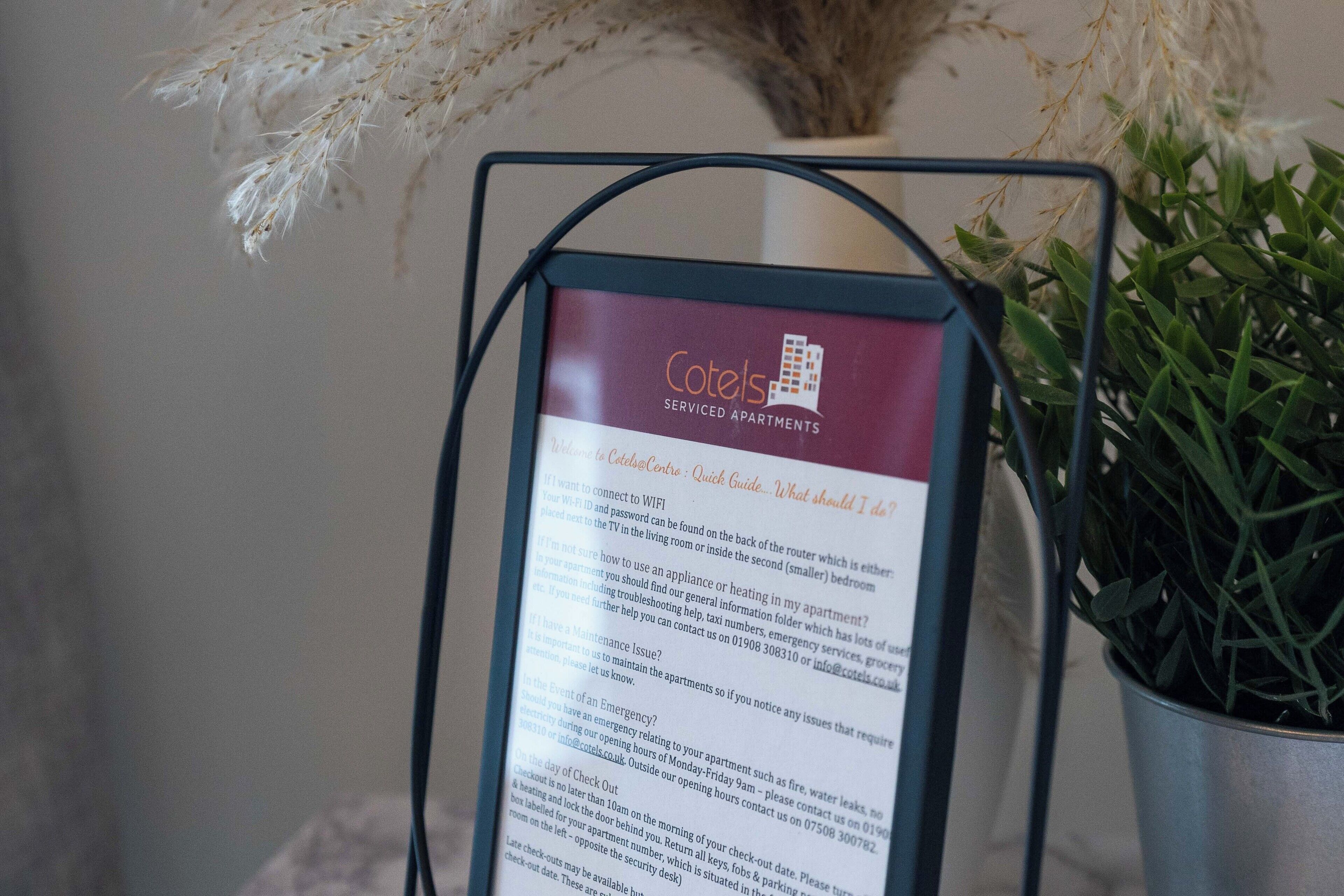 A signboard with information about Cotels Serviced Apartments, including WiFi, emergency contact, and check-out procedures.