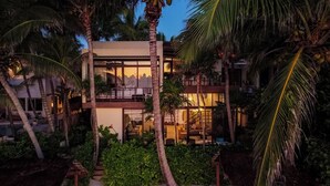 A modern two-story building with large windows, surrounded by lush greenery and palm trees. - Ocean Front Villa @ Private Beach in Tulum. Snorkel, Kayak, Paddleboard Included (Tulum)
