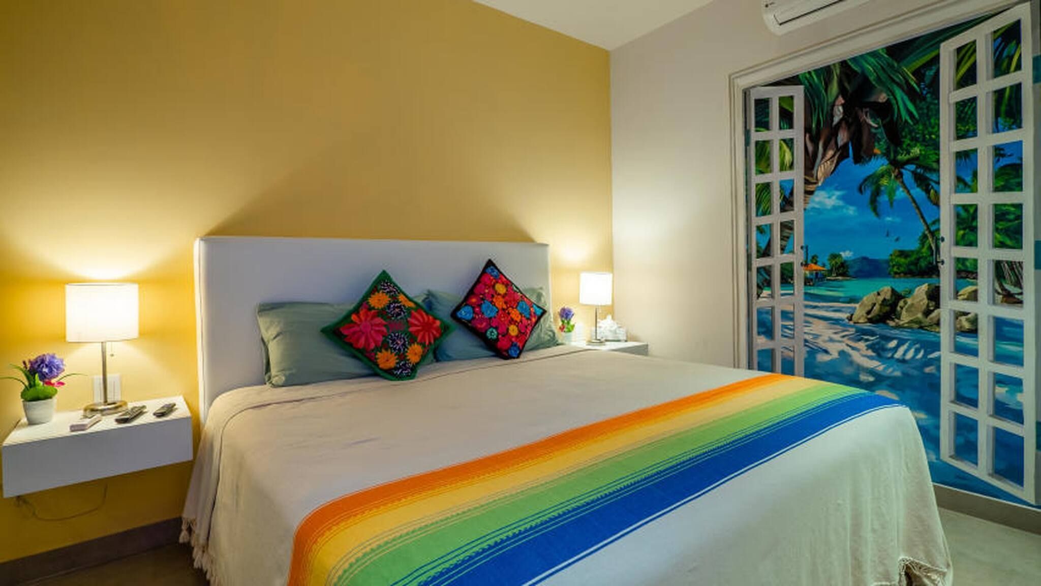 A hotel room with a bed, two nightstands, a lamp, and a window with a view of a beach.