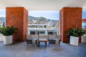 A terrace with two chairs and a table, brick walls, potted plants, and a view of a cityscape.