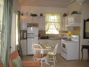 A compact kitchen with white cabinets, a dining table with chairs, a microwave, and a stove. - Cherry Garden Villa Apartment - private pool in desirable Rockley Beach location (Rockley, Christ Church)