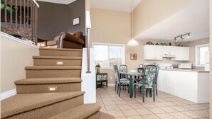 A staircase with carpeted steps leading to a living area with a dining table and chairs.