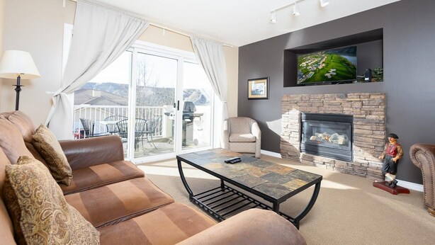 A living room with a sofa, a fireplace, a television, and a balcony with outdoor furniture.
