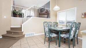 A dining area with a round table and six chairs, a staircase with a railing, and a window with blinds.