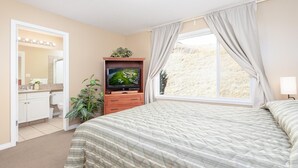 A bedroom with a bed, a TV, a dresser, a mirror, and a window with curtains. - Paradise Canyon Golf Resort - Luxury Condo U409 (Lethbridge)