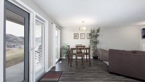 Een moderne woonkamer met een eethoek, een bank en een groot raam met zonwering.