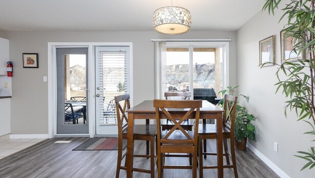 Een eetruimte met een houten tafel en stoelen, een hanglamp en uitzicht op een bergachtig landschap door grote ramen.