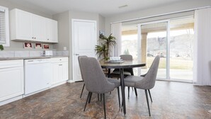 Une cuisine moderne avec des meubles blancs, une table à manger entourée de quatre chaises et une grande porte-fenêtre coulissante donnant sur une vue imprenable sur une montagne.