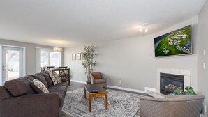 A spacious living room with a large sectional sofa, a coffee table, and a fireplace. There is a dining area in the background and a large window providing natural light. - Paradise Canyon Golf Resort - Signature Villa 380 (Lethbridge)