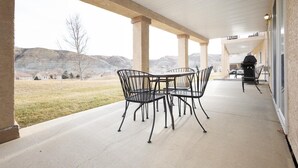 A covered patio with a table and chairs, a grill, and a view of a grassy field and hills. - Paradise Canyon Golf Resort - Signature Villa 380 (Lethbridge)