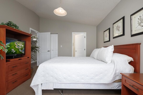 Un dormitorio con una cama, un televisor sobre un mueble de madera y obras de arte enmarcadas en la pared.