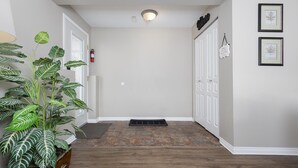 Un pasillo con suelo de madera, una planta en maceta, un extintor, una puerta y un cuadro en la pared.