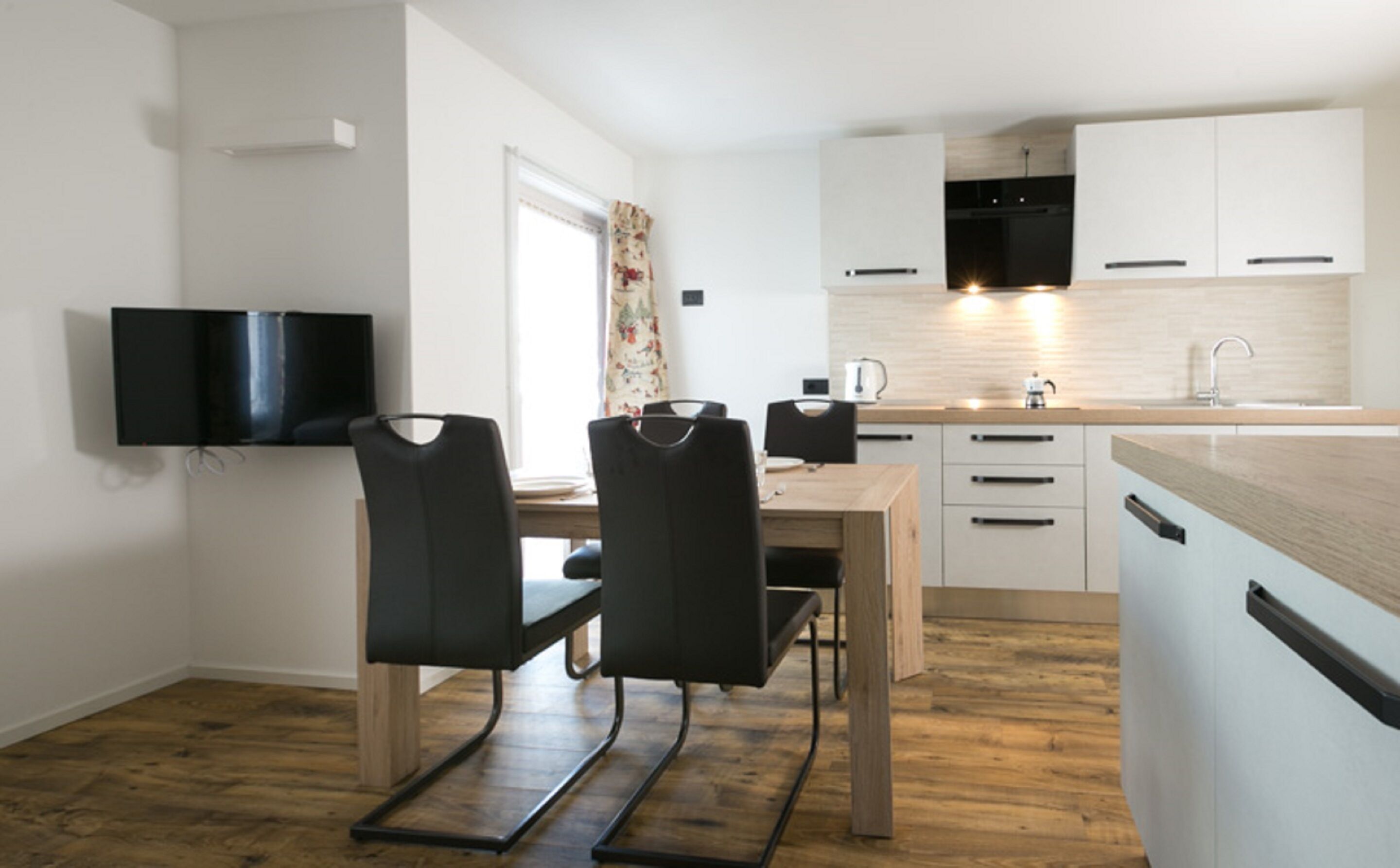 A modern kitchen with white cabinets, a wooden countertop, and a black TV mounted on the wall.