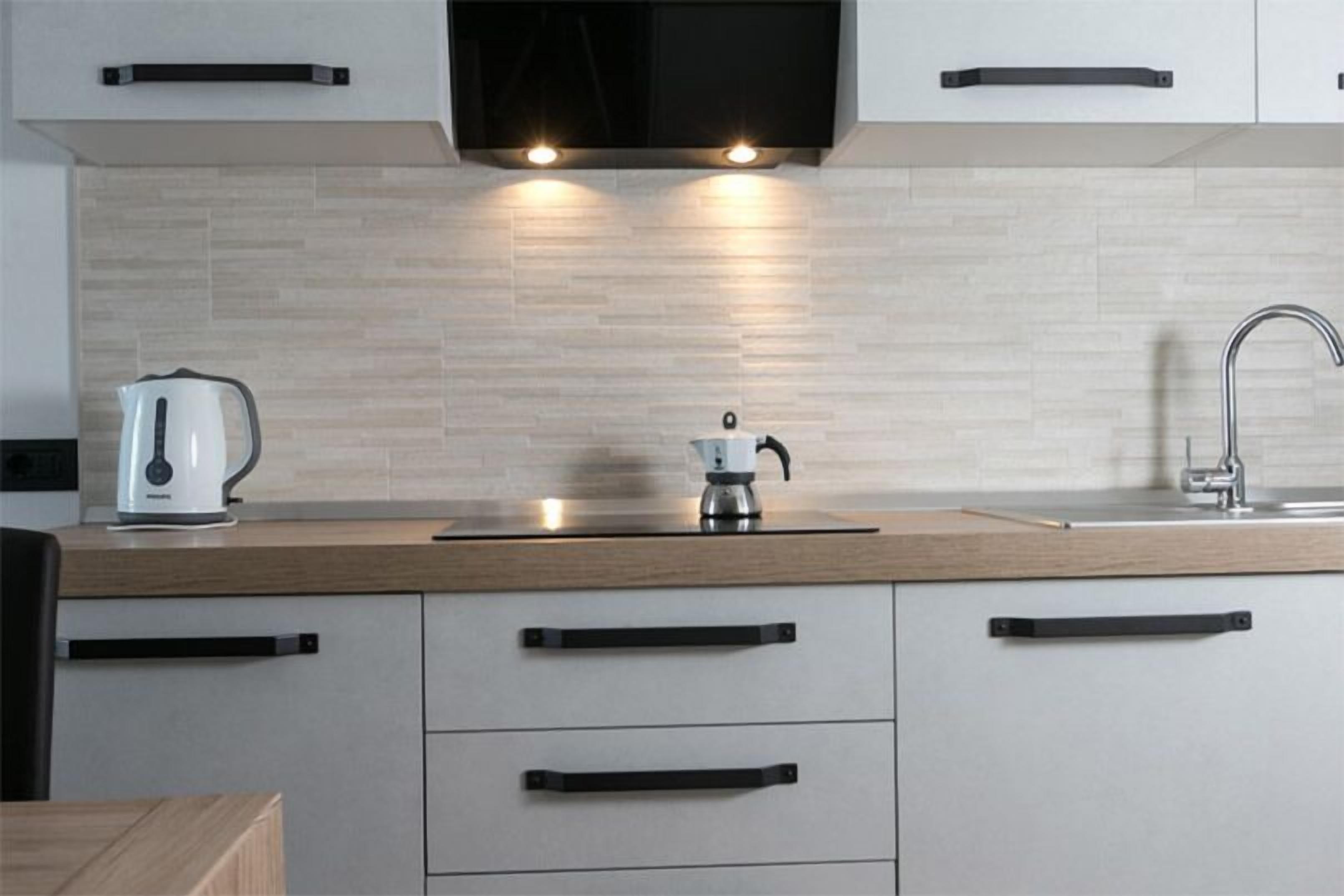 A modern kitchen with a wooden countertop, white cabinets, a black range hood, and a stainless steel kettle.