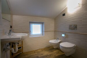 Bagno con lavandino, bidet, water e pavimento in legno, con una finestra.