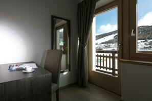 Een hotelkamer met een houten bureau, een stoel, een raam met uitzicht op een besneeerd landschap en een deur met houten omlijsting.