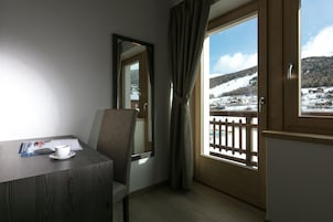 Una camera d'albergo con una scrivania in legno, una sedia, una finestra che si affaccia su un paesaggio innevato e una porta con stipite in legno.