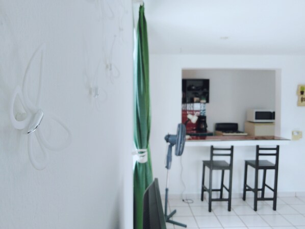 A room with a white wall, a green curtain, a desk with a computer, and two chairs.