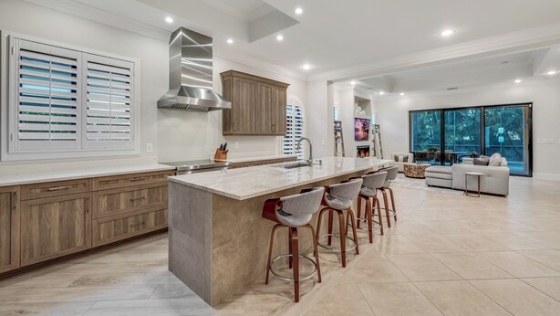 Una cocina moderna con una isla grande, taburetes de bar y un comedor con sofá y mesa.