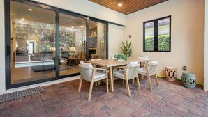 Un patio con mesa y sillas de madera, una puerta de cristal que da a una zona de piscina y un ventilador de techo.