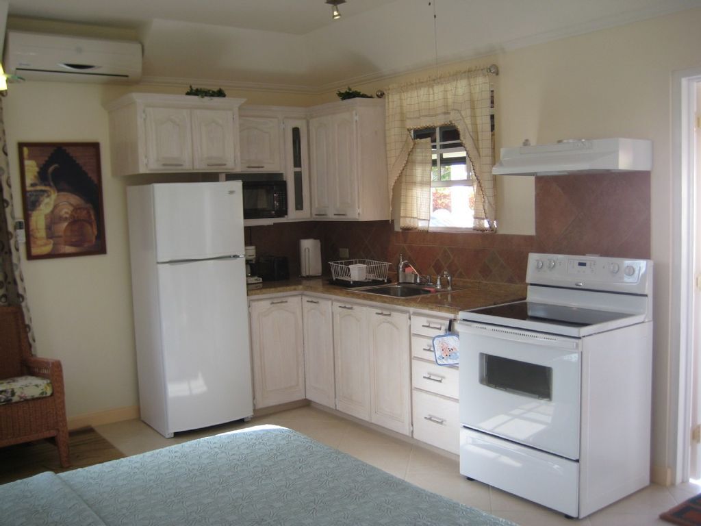 A compact kitchen with white cabinets, a refrigerator, a microwave, an oven, and a sink.