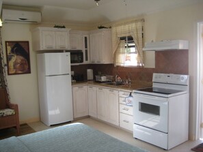 A compact kitchen with white cabinets, a refrigerator, a microwave, an oven, and a sink.