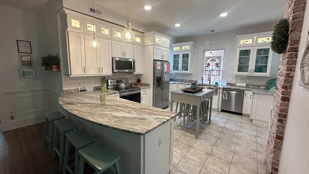A modern kitchen with white cabinets, a large island with stools, stainless steel appliances, and a decorative stained glass window. - Renovated Gem: Walk to Beach, Historic District Shops, Restaurants, Central Park (Cape Charles)
