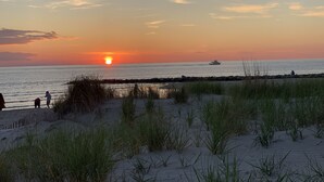 A beach at sunset with a boat in the distance and people walking along the shore. - Renovated Gem: Walk to Beach, Historic District Shops, Restaurants, Central Park (Cape Charles)
