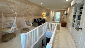 A cozy room with a hanging chair, a sofa with cushions, a wooden floor, and a white railing. - Renovated Gem: Walk to Beach, Historic District Shops, Restaurants, Central Park (Cape Charles)