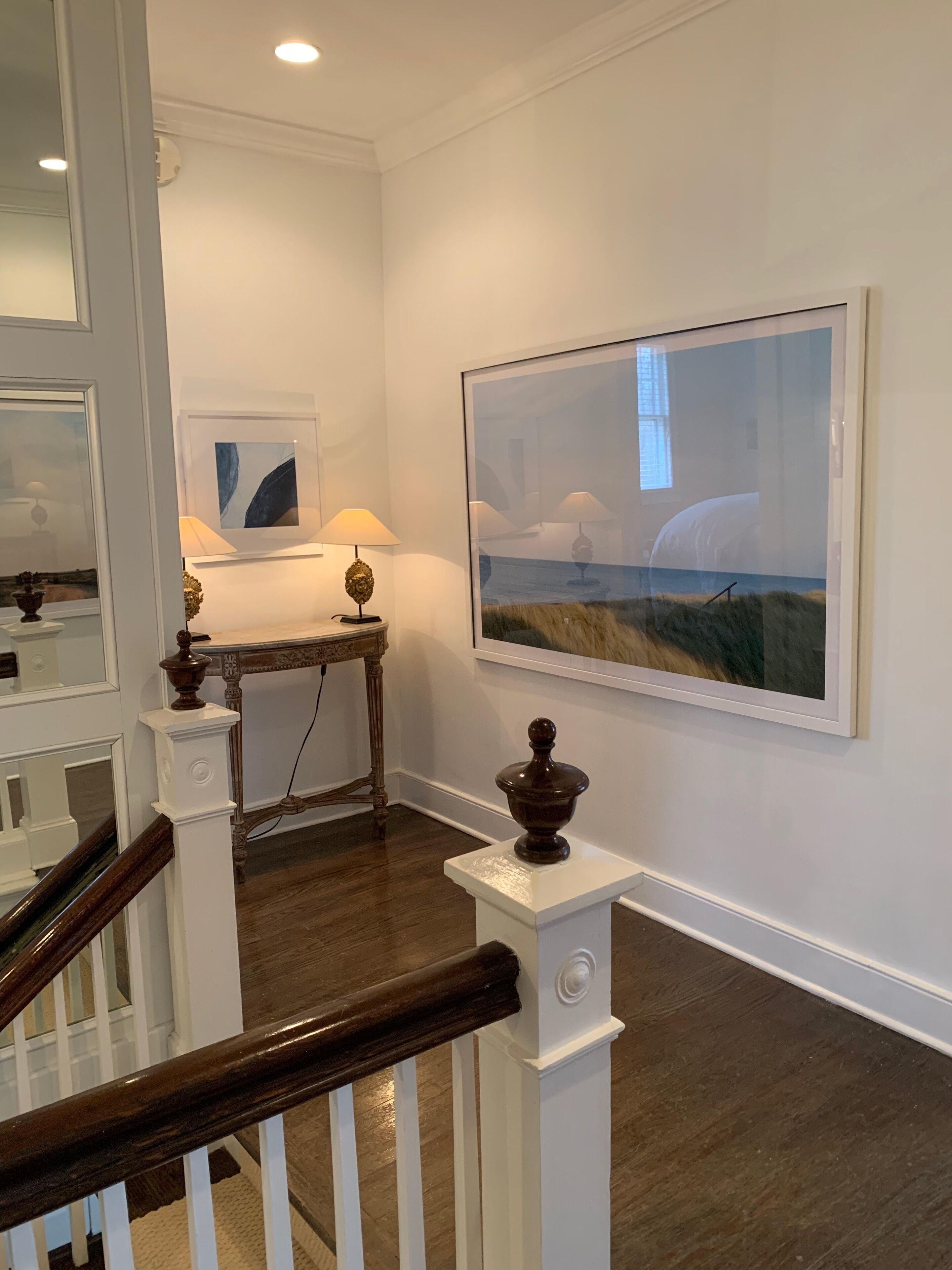 A staircase with a wooden handrail, a small table with a lamp, and a framed picture on the wall.