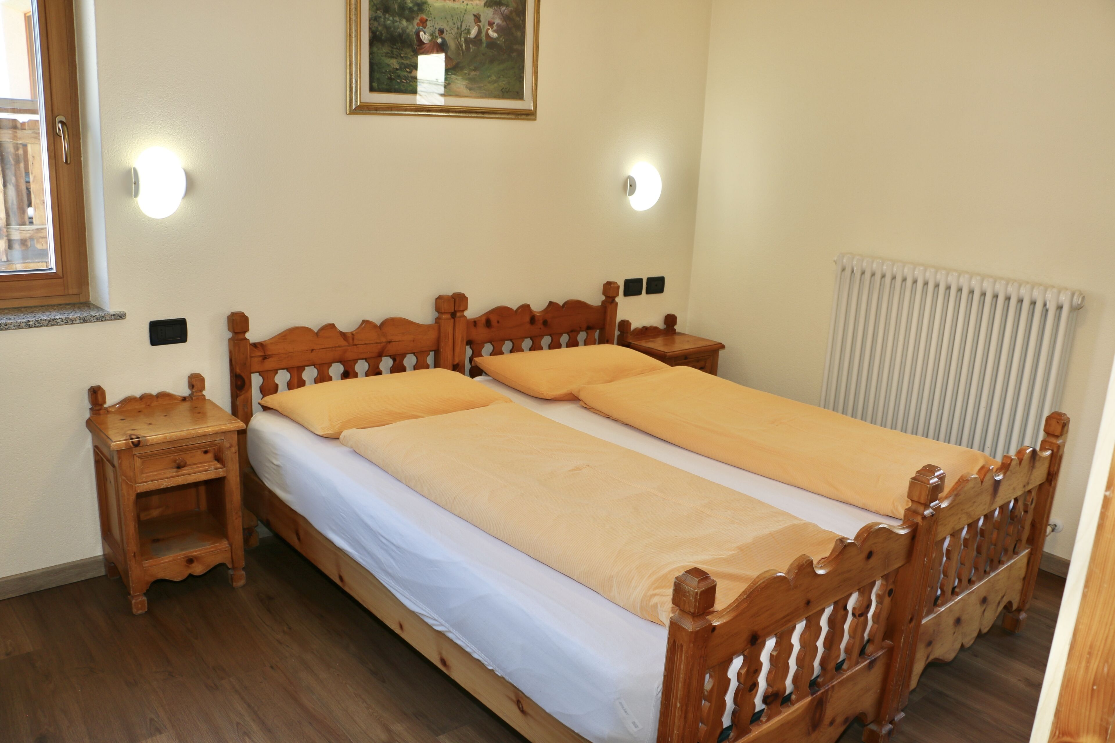 A double bed with wooden headboard and footboard, two bedside tables, and a radiator.