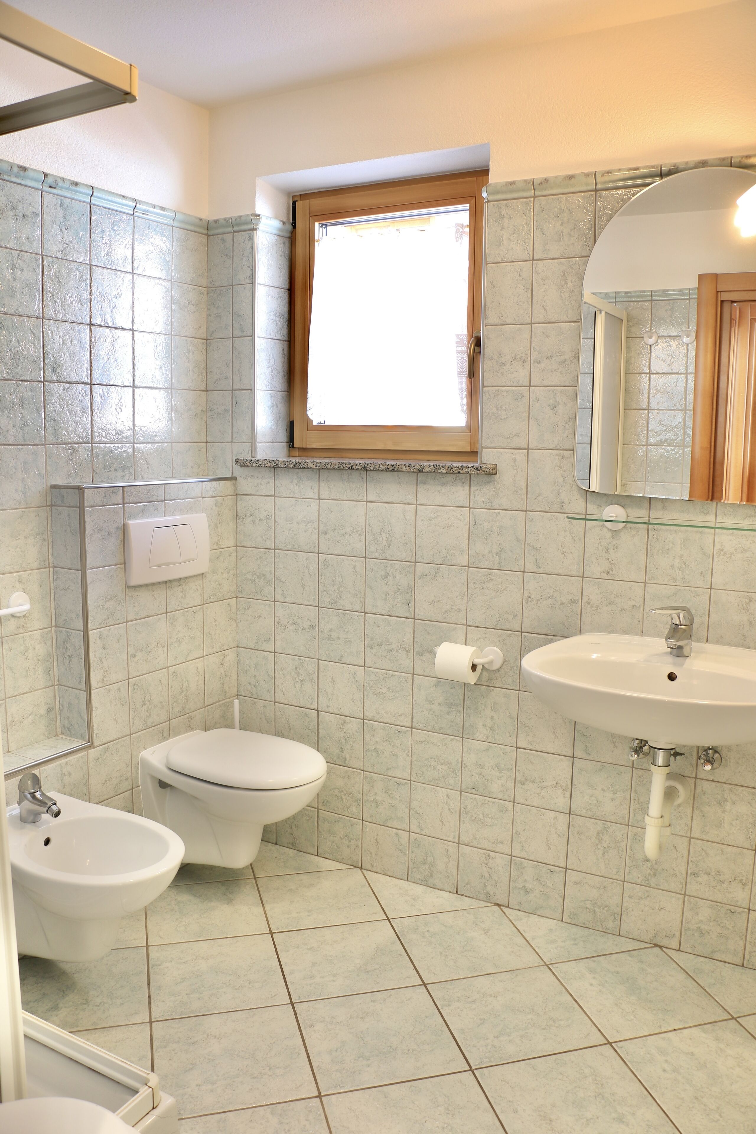 Un baño con inodoro, bidé, lavamanos y ventana.