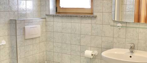 A bathroom with a toilet, bidet, sink, and a window.