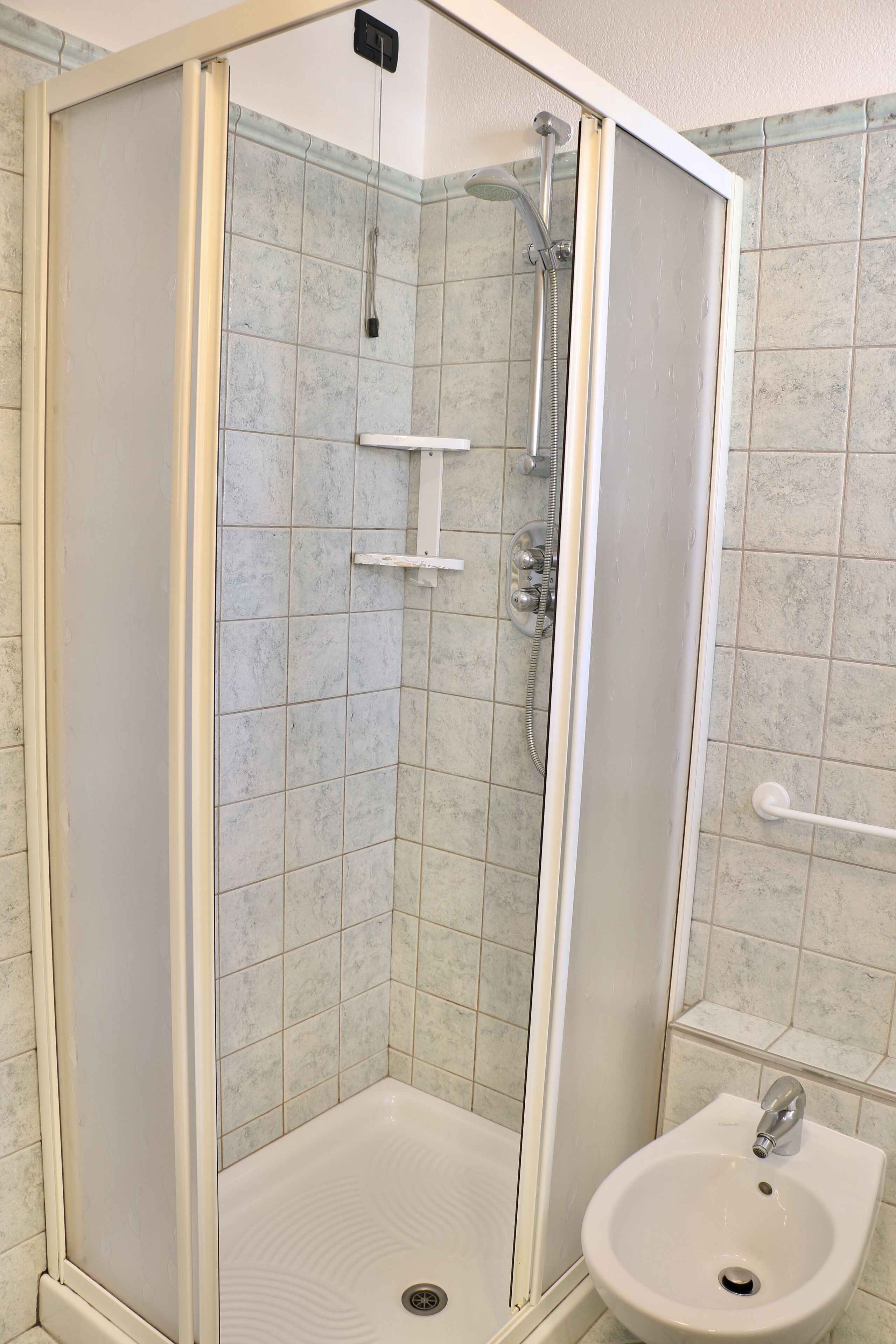 A glass-enclosed shower with a white sink and a handheld showerhead.