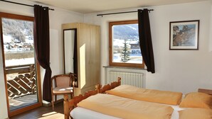 Una habitación con dos camas, una silla de madera, un ventanal con vistas a montañas nevadas y un radiador.