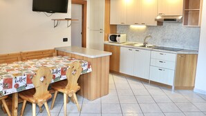 Cocina compacta con armarios de madera, microondas, lavamanos y comedor con mesa y sillas.