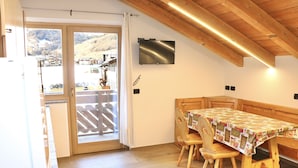 Un comedor con una mesa y sillas de madera, un televisor montado en la pared y vistas a un paisaje montañoso a través de un ventanal.