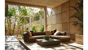 A sunlit outdoor seating area with a sofa and a coffee table, surrounded by plants and a tiled wall. - CASA T -  Chic, Modern Villa with 3 Master Suites, AC & Pool  (Tulum)