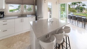 Cozinha moderna com uma ilha grande, armários brancos e vista para o exterior.