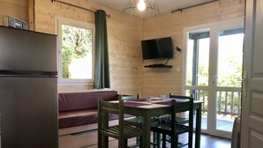 A wooden cabin interior with a dining table, chairs, a sofa, a TV, and a refrigerator.